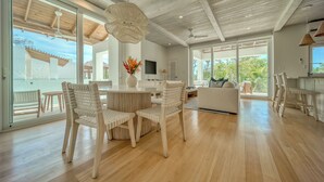 A spacious living area with a wooden floor, white furniture, and large windows offering a view of the outdoors. - Elegant 3-Bed, 3-Bath Penthouse with Panoramic Ocean Views at Watercolors (Roatán)