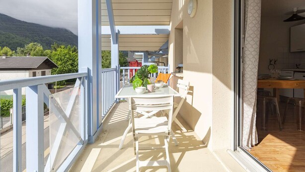 Ein Balkon mit Tisch und Stühlen, Blick auf die Berge und ein durch offene Tür sichtbarer Küchenbereich.
