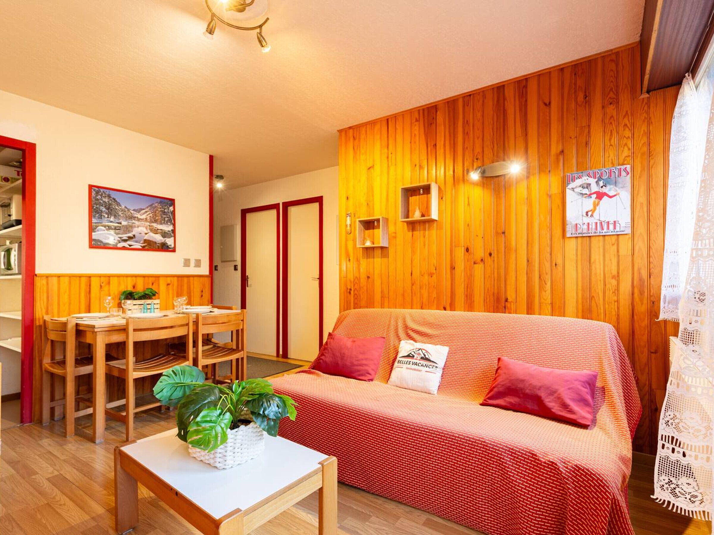 Un salon chaleureux avec un mur en bois, un canapé, une table à manger avec des chaises et une petite table sur laquelle est posée une plante.