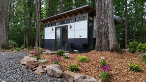 Une cabane moderne dotée d’une grande porte-fenêtre coulissante, entourée d’une forêt.