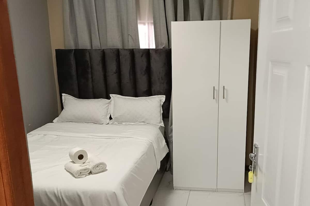 A bedroom with a bed, white curtains, a wardrobe, and a door.