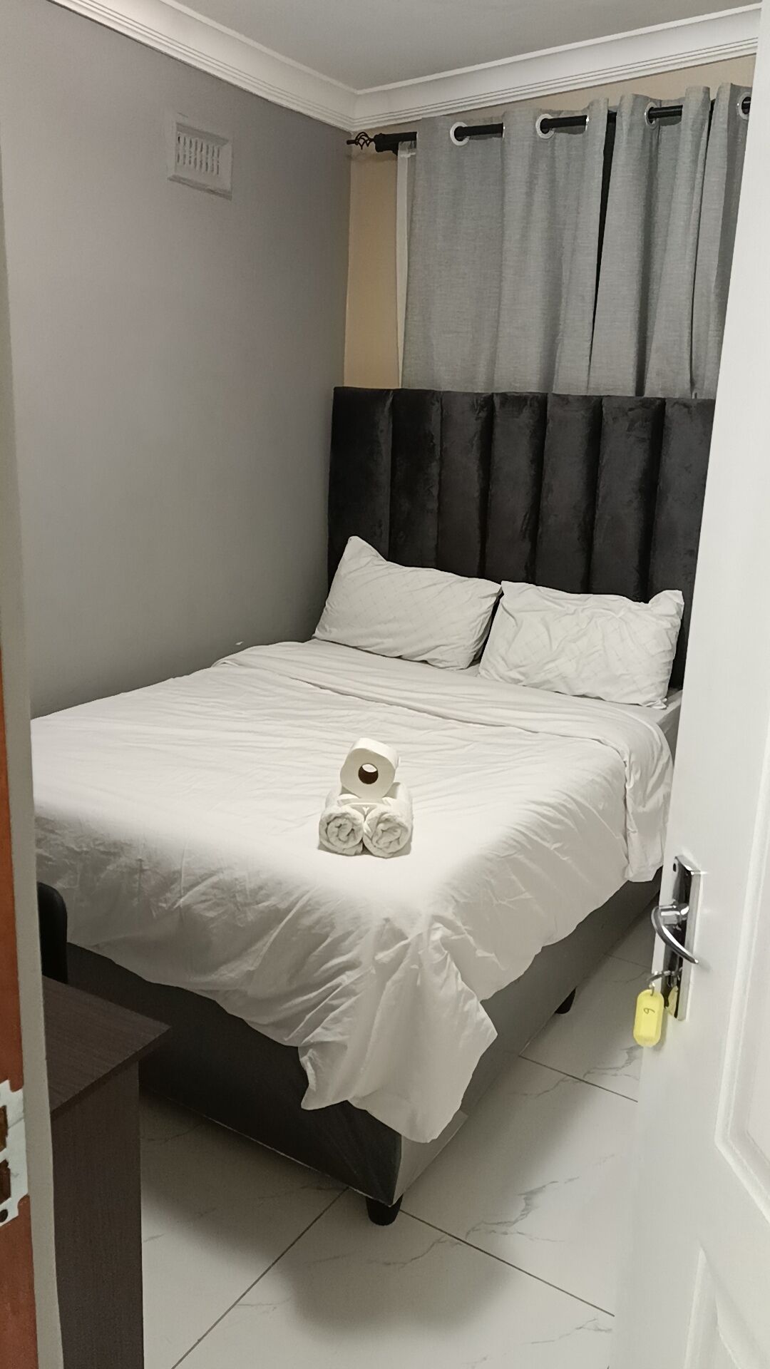 Ein ordentlich bezogenes Bett mit weißen Leinentüchern, einem schwarzen Kopfteil und einem Paar zusammengerollter Handtücher.
