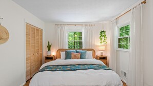A bedroom with a wooden bed, white walls, a window with curtains, and a bedside plant.