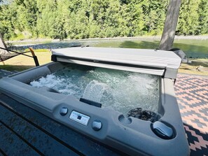 Ein Whirlpool mit Bedienfeld, umgeben von einer Holzterrasse und Blick auf einen Fluss.