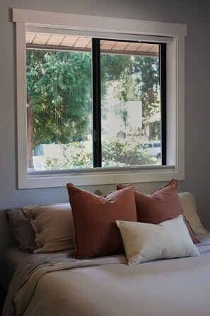 Ein Schlafzimmer mit Bett, Kissen und einem Fenster mit Blick auf Grünfläche.