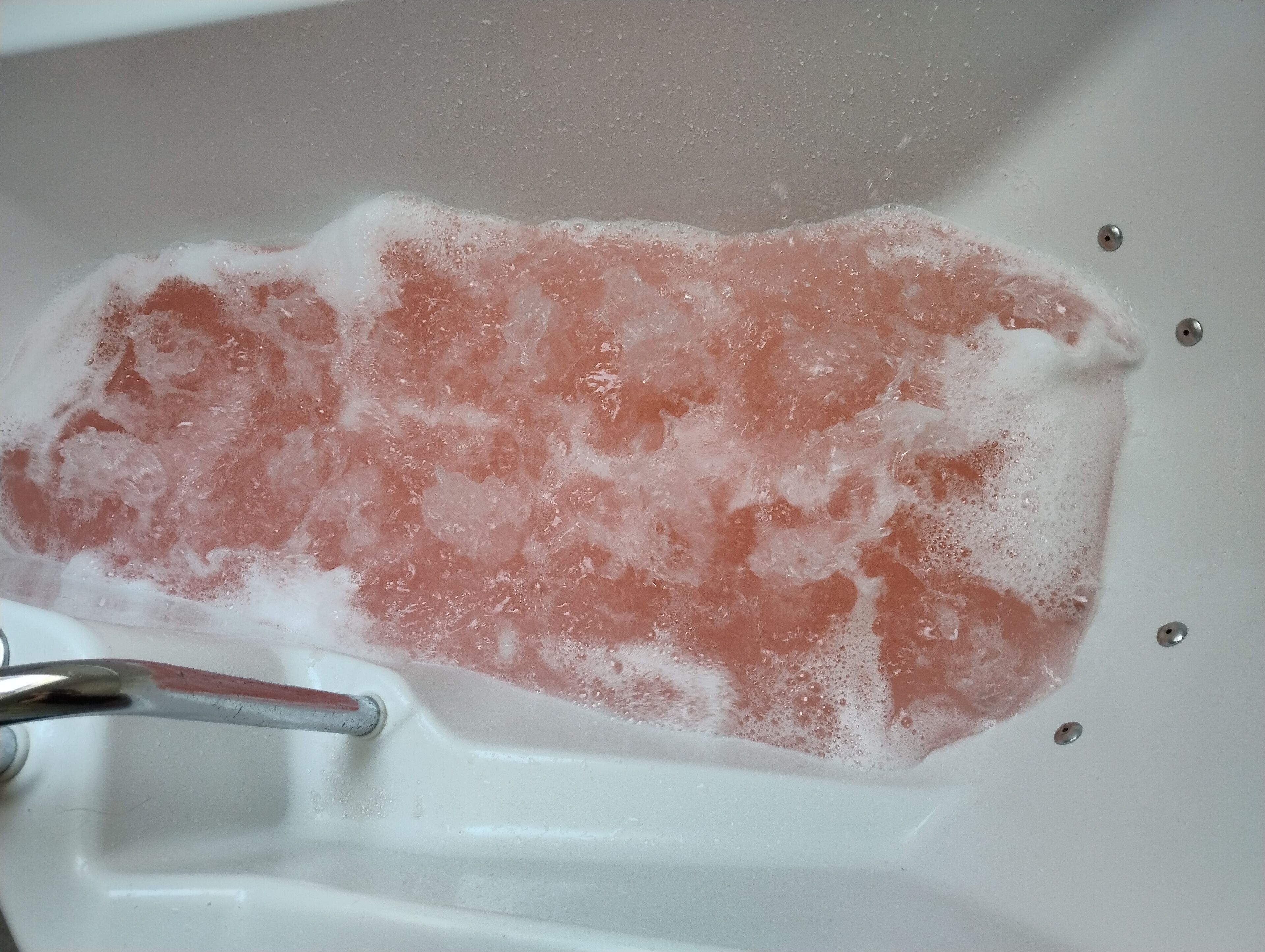 Una bañera llena de sales de baño rosas y burbujas.
