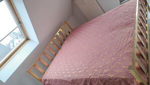 Une pièce avec un plafond haut, un lit superposé, une fenêtre et un radiateur.