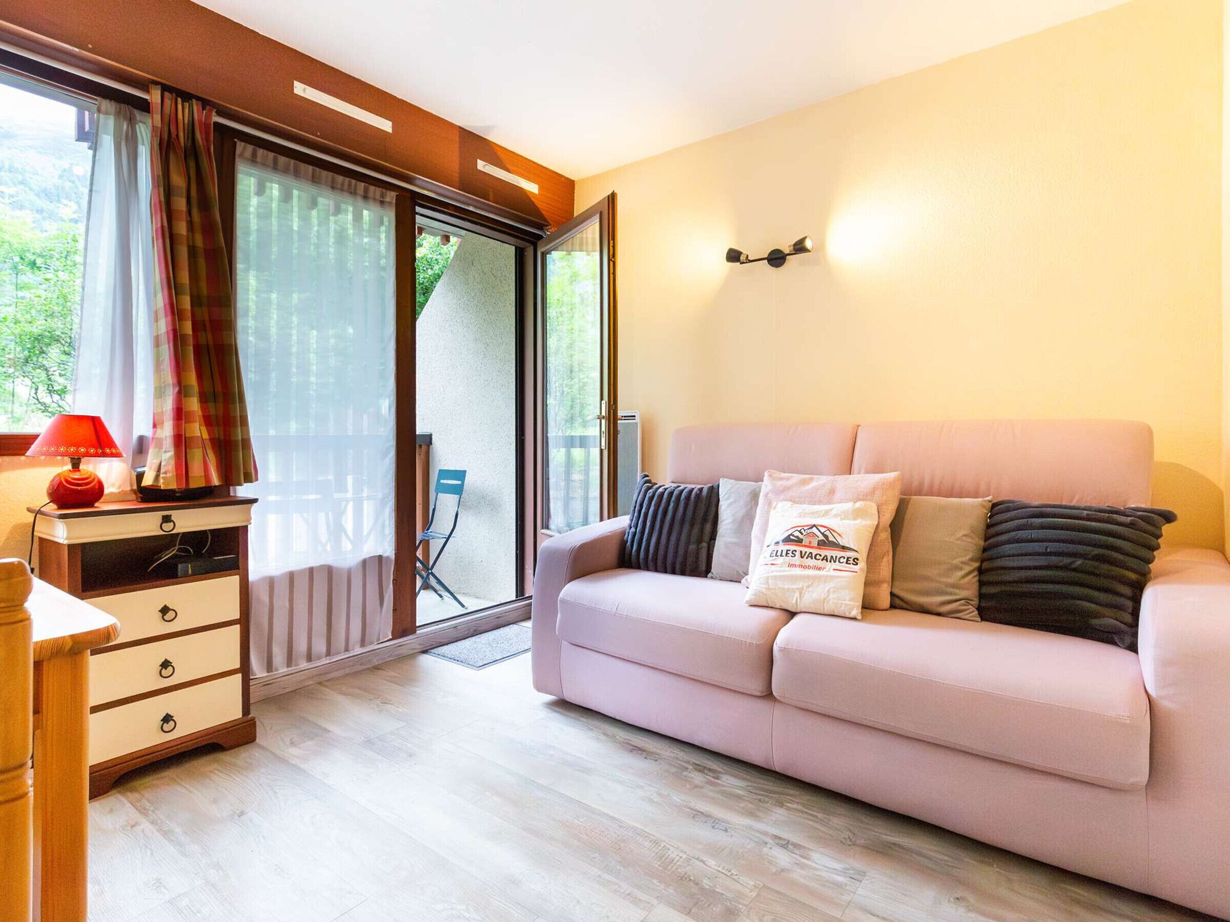 Ein modernes Wohnzimmer mit einer Couch, einem Holztisch und einer Lampe. Eine Glasschiebetür führt in einen Außenbereich.