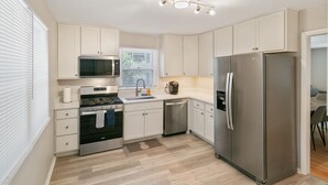 A modern kitchen with white cabinets, stainless steel appliances, a microwave, oven, sink, and a refrigerator. - Bright & Roomy 5BR – Family-Ready Near Naval Base! (Libertyville)