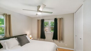 A bedroom with a bed, a ceiling fan, a nightstand with a lamp, and a window with curtains. - Bright & Roomy 5BR – Family-Ready Near Naval Base! (Libertyville)