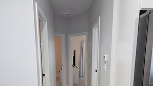 Um corredor com chão de madeira, paredes brancas e uma geladeira de aço inoxidável à direita.
