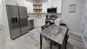 Cozinha moderna com armários brancos, eletrodomésticos de aço inoxidável e uma mesa de jantar de madeira.
