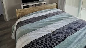 Quarto com cama, televisão sobre suporte, ventoinha no teto e janela com cortinas.