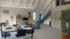 A modern dining area with a white table, black chairs, and a blue plate with lemons. There is a staircase leading to an upper level. - Charming 3-bedroom house in Figueira da Foz, Serra da Boa Viagem (Quiaios)