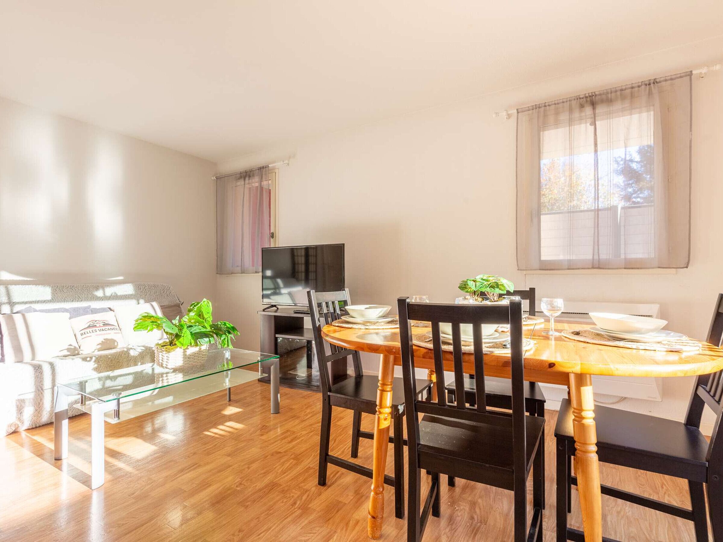 A dining area with a wooden table, black chairs, a glass coffee table, and a television on a stand.