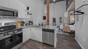 A modern kitchen with stainless steel appliances, a dishwasher, and a microwave. There is a wooden beam ceiling and a hanging light fixture. - Oregon District I Spacious I Free Parking (Dayton)