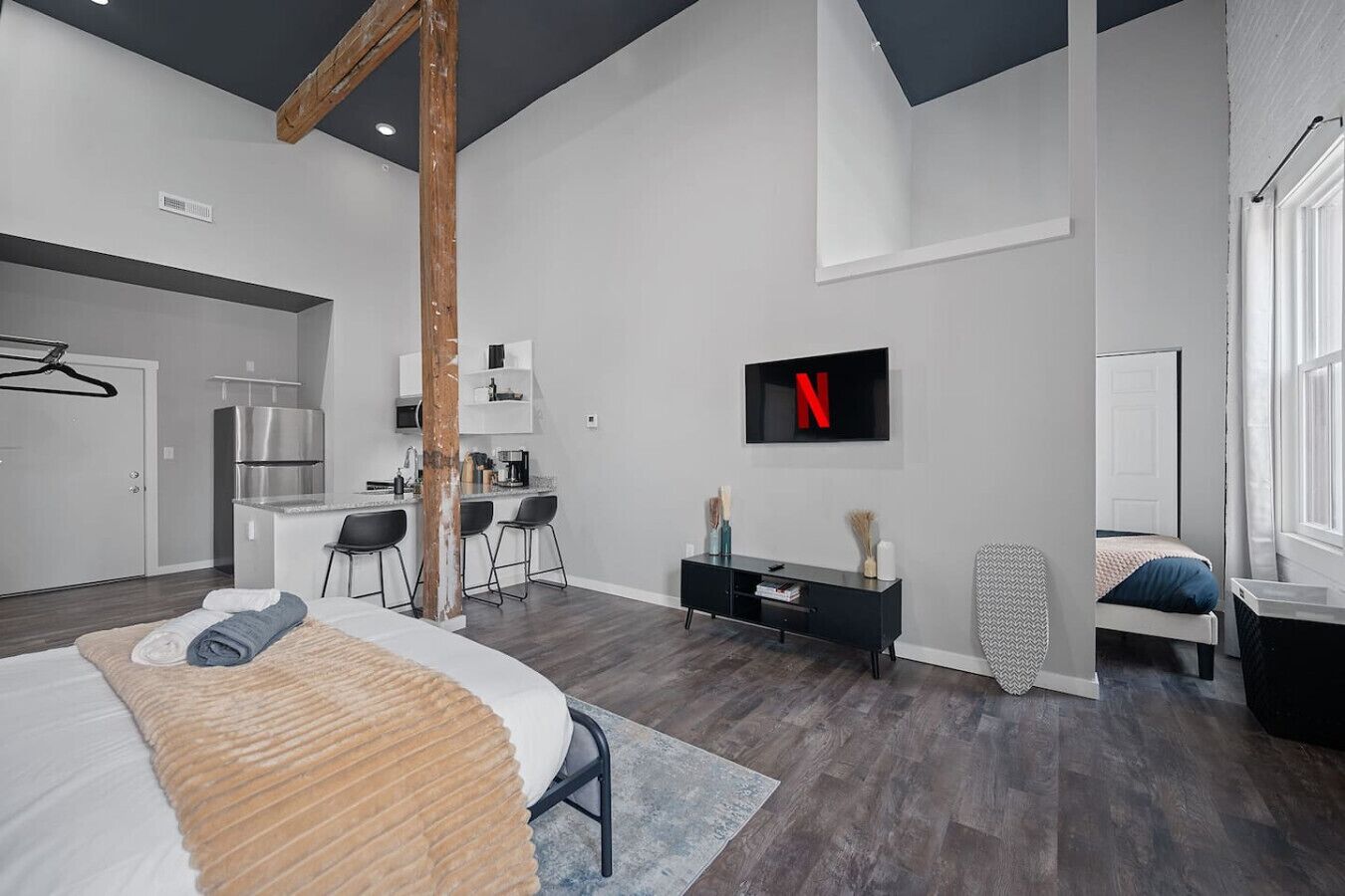 Una habitación de hotel moderna con una cama grande, un escritorio, una kitchenette y un televisor montado en la pared.