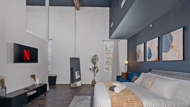 A modern bedroom with a large bed, a TV mounted on the wall, and artwork on the walls. - Oregon District I Spacious I Free Parking (Dayton)