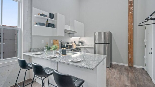 A modern kitchen with a granite countertop, stainless steel appliances, and black bar stools.