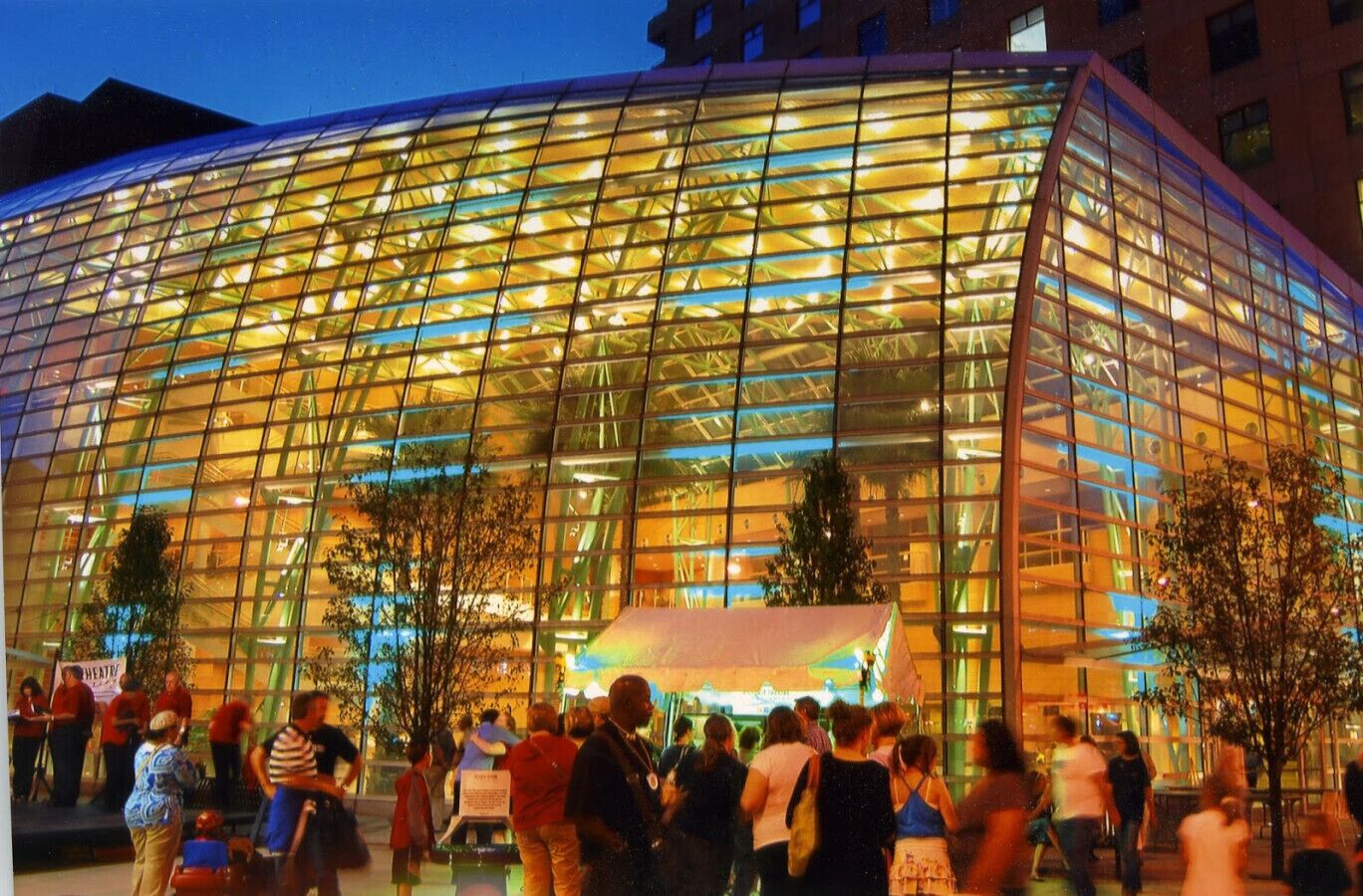A modern glass building with a curved facade, surrounded by a crowd of people.