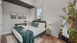 A modern bedroom with a large bed, a nightstand, a mirror, and a potted plant.