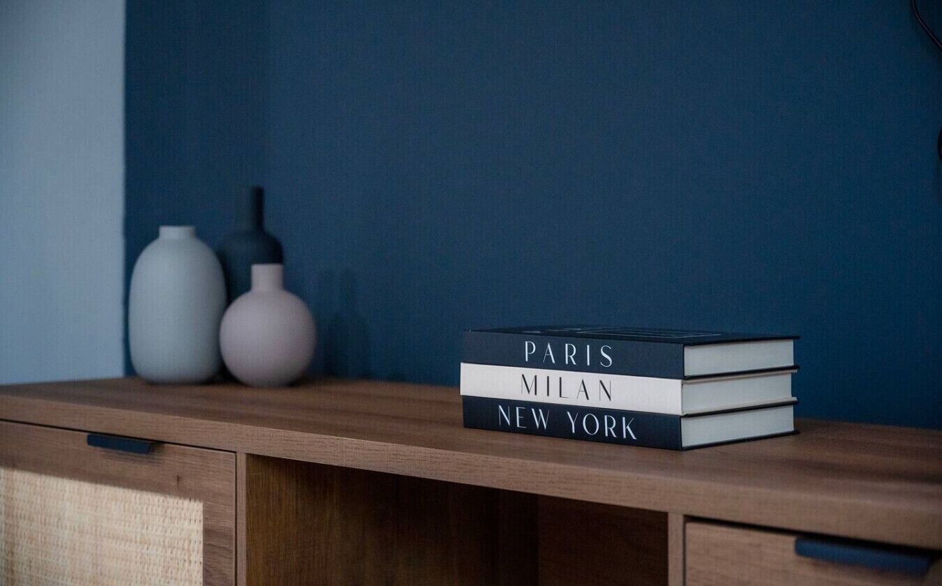 Ein Stapel Bücher mit dem Titel "PARIS MILAN NEW YORK" auf einer Holzoberfläche.