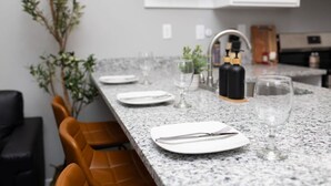 Una cocina con encimera de granito, armarios blancos y un comedor con sillas.