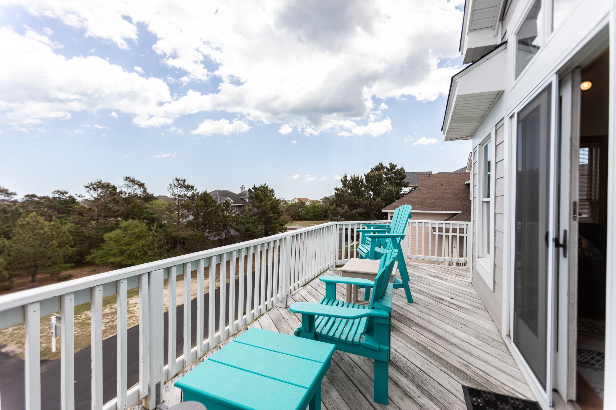 A deck with a white railing, turquoise Adirondack chairs, and a table.