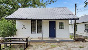 A small, single-story building with a dark blue door, two windows with black shutters, and a metal roof. - Tenkiller Pine Cabin Escape Near Lake Adventures A (Cookson)