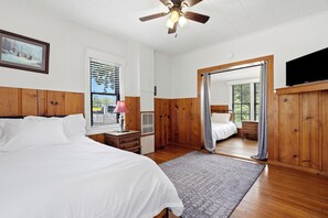 A bedroom with a bed, a desk, a lamp, a ceiling fan, and a television.
