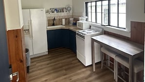 A compact kitchen with a refrigerator, microwave, stove, and sink. There is a window providing natural light and a wooden bench at the counter. - Tenkiller Pine Cabin Escape Near Lake Adventures A (Cookson)