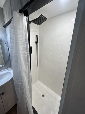 A modern bathroom with white tiled walls, a glass shower enclosure, and a white sink.