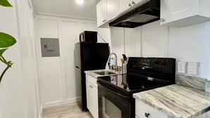 Una cucina compatta con mobili bianchi, un fornello nero e un forno a microonde.