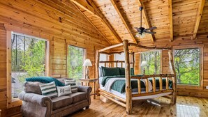 A wooden cabin interior with a bed, a sofa, and large windows.