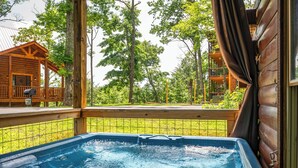 Un bain à remous avec une terrasse en bois et une vue sur un chalet en bois et des arbres.