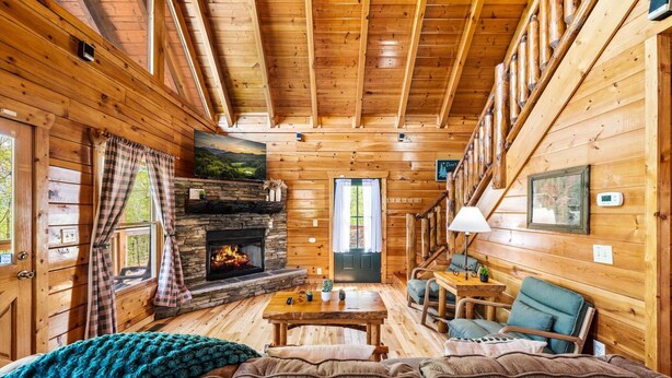 A log cabin interior with a stone fireplace, wooden walls, a sofa, a table, and a chair.