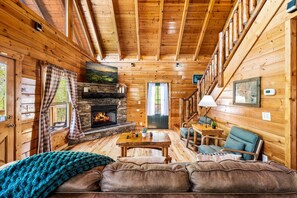 A log cabin interior with a stone fireplace, wooden walls, a sofa, a table, and a chair. - Gatlinburg Retreat:  Hot Tub, Game Room & Pool (Gatlinburg)