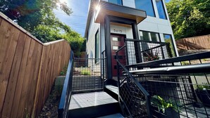 Een modern, twee verdiepingen hoog gebouw met zichtbaar huisnummer 5615, een houten omheining en een metalen trap die naar de ingang leidt.