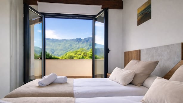 A bedroom with two beds, a view of mountains, and a balcony.
