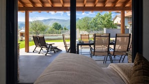 A bedroom with a wooden ceiling and a view of a patio with outdoor furniture and a table.