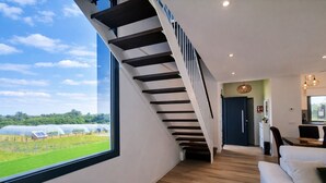 A modern interior with a staircase leading to a dining area, a large window with a view of greenhouses, and a cozy seating area.