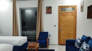 A modern hotel room with a large bed, a blue sofa, a blue armchair, a wooden coffee table, and a wooden door. - Dar naima  (Essaouira)