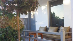 A modern outdoor seating area with a sofa and a small table, surrounded by a wooden fence and lush greenery. - Dar naima  (Essaouira)
