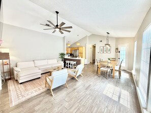 A spacious living area with a sofa, coffee table, and chairs, a kitchen with wooden cabinets, and a dining area with a table and chairs.