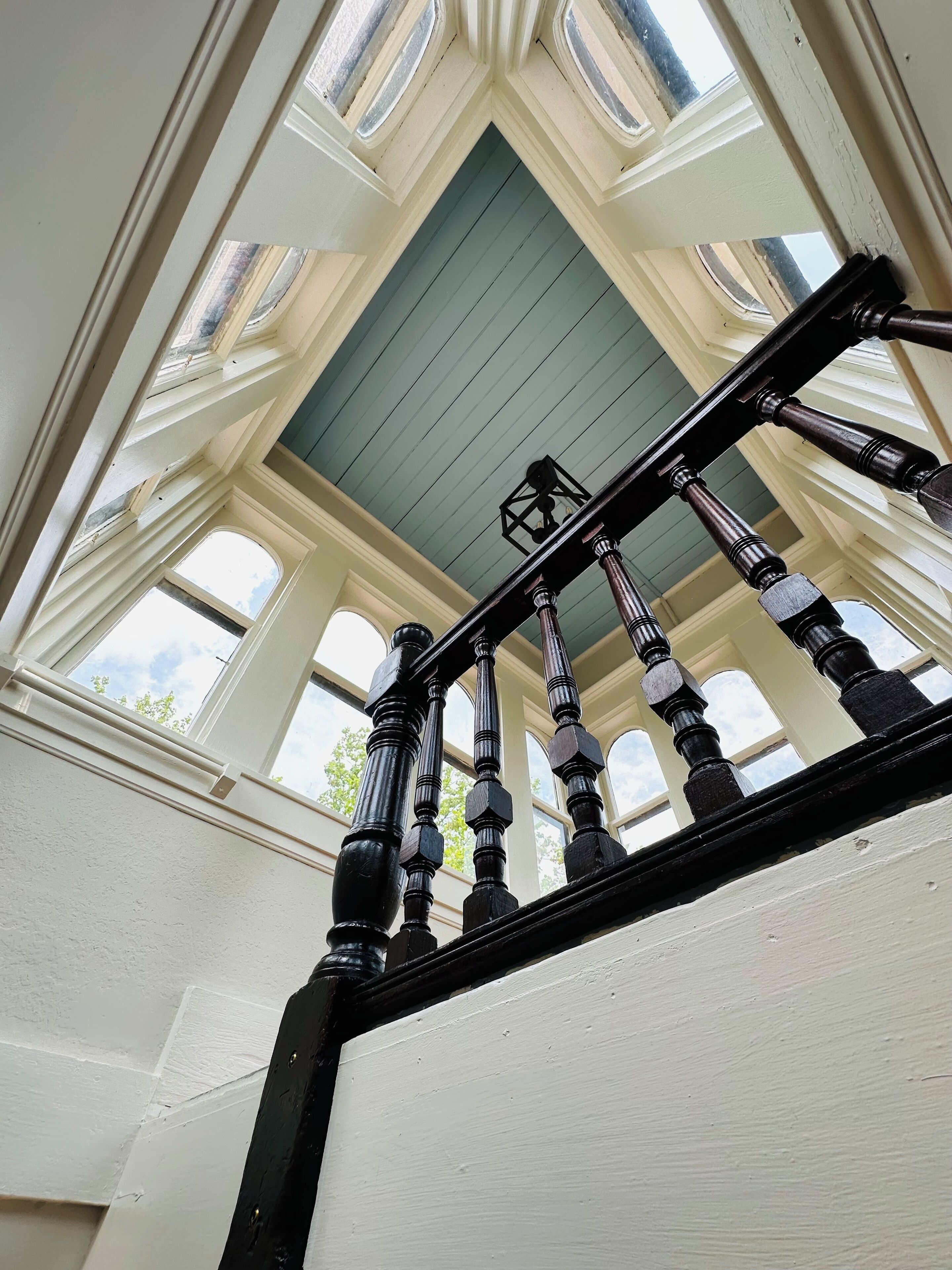 A staircase with a black balustrade leading to a room with a green ceiling and multiple windows.