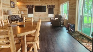 Interior de una cabaña de madera con una mesa de comedor, sillas, un sofá y un sillón reclinable.