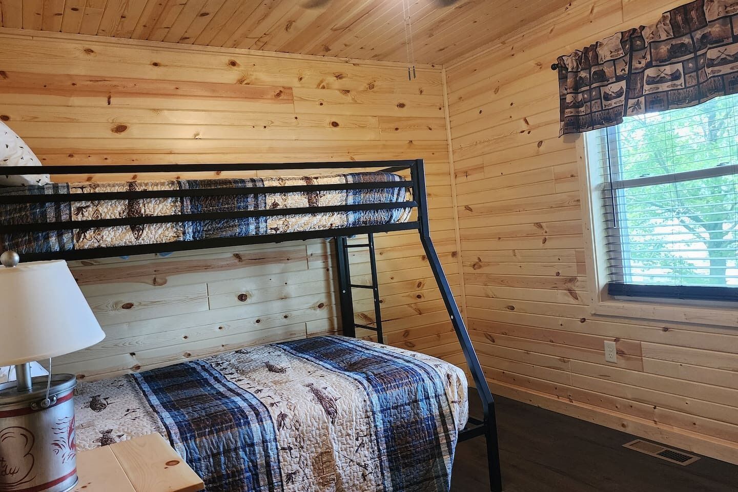 Un lit superposé avec une tête de lit, une lampe de chevet et une fenêtre avec des stores.
