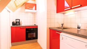 Una cucina compatta con mobili rossi, lavastoviglie, piano cottura e macchina del caffè.