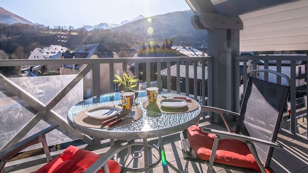 Un balcone con un tavolo rotondo apparecchiato per mangiare, sedie e vista sulle montagne.