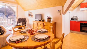 Una zona pranzo accogliente con un tavolo di legno apparecchiato per quattro persone, una televisione su un mobile e una cucina con mobili rossi.